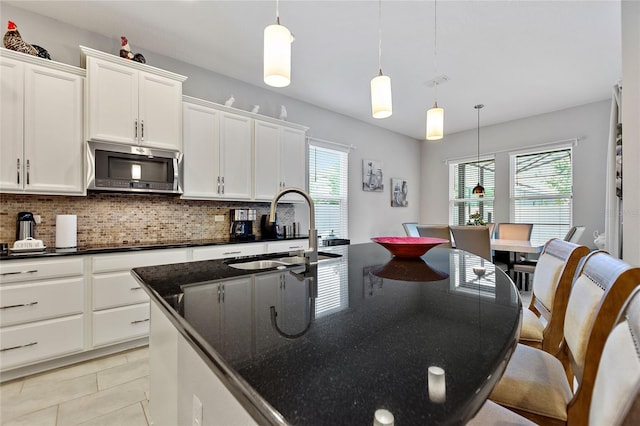 kitchen with white cabinetry, sink, hanging light fixtures, and an island with sink