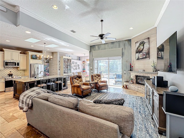 living room featuring crown molding, ceiling fan, a brick fireplace, and a textured ceiling