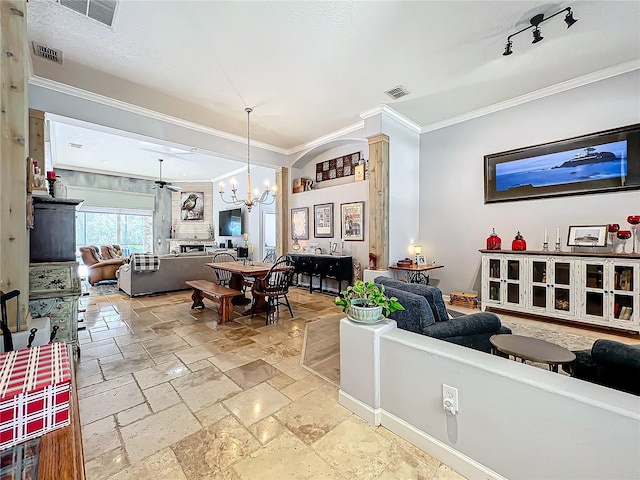 living room featuring crown molding, rail lighting, ceiling fan with notable chandelier, and ornate columns