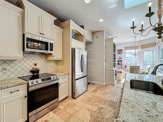 kitchen with pendant lighting, sink, appliances with stainless steel finishes, a notable chandelier, and cream cabinets