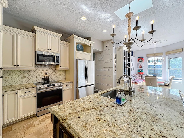 kitchen featuring sink, stainless steel appliances, cream cabinets, decorative light fixtures, and a chandelier