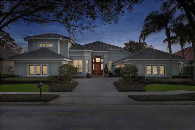 mediterranean / spanish house featuring stucco siding, a tiled roof, and decorative driveway