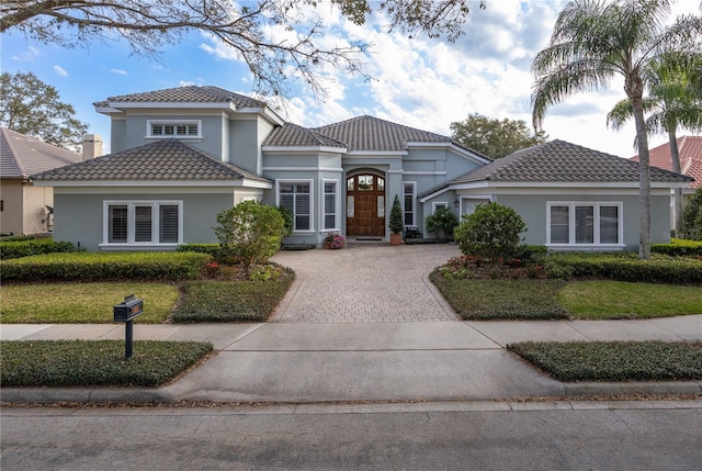 mediterranean / spanish-style home featuring a tiled roof, decorative driveway, and stucco siding