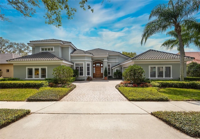 mediterranean / spanish house featuring stucco siding, a tiled roof, decorative driveway, and a front yard