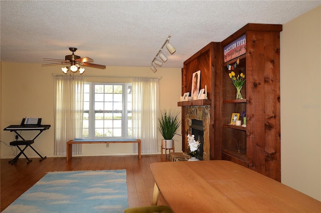 dining area with a stone fireplace, wood-type flooring, a textured ceiling, and track lighting