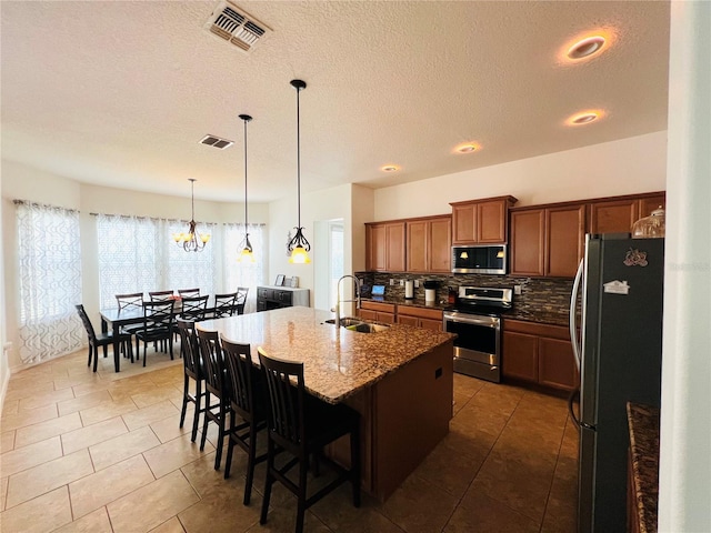 kitchen featuring a breakfast bar, sink, hanging light fixtures, stainless steel appliances, and a center island with sink