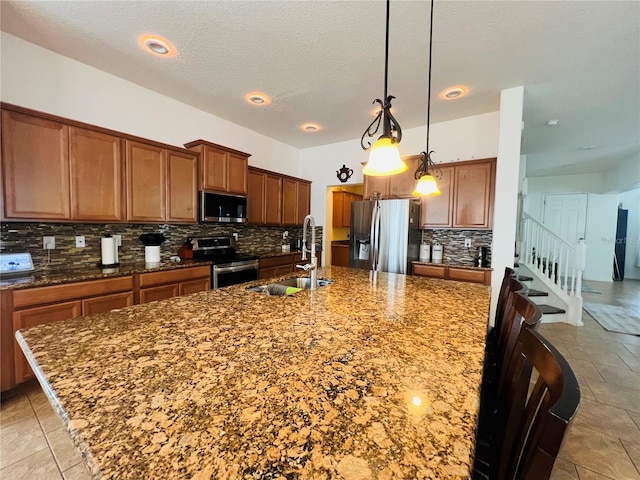 kitchen with sink, tasteful backsplash, hanging light fixtures, a center island with sink, and stainless steel appliances