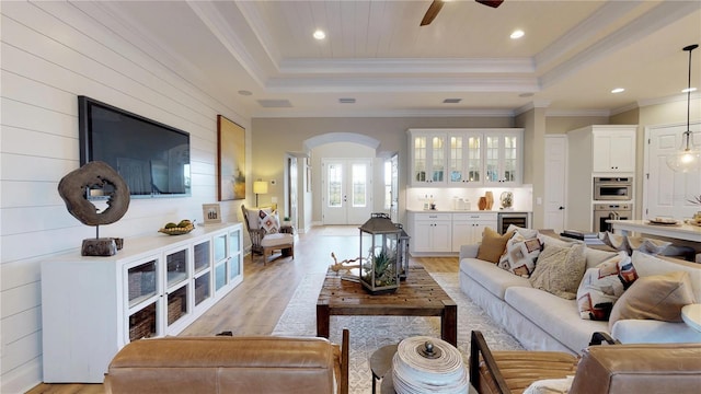 living room featuring a raised ceiling, ornamental molding, beverage cooler, and light wood-type flooring