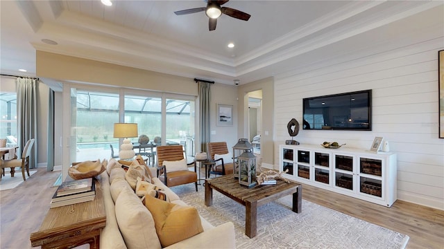 living room featuring crown molding, ceiling fan, a raised ceiling, and light hardwood / wood-style floors