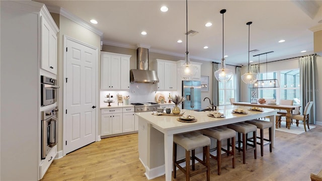 kitchen featuring white cabinets, stainless steel appliances, hanging light fixtures, and wall chimney exhaust hood