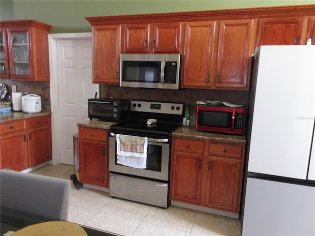 kitchen with tasteful backsplash, light tile patterned floors, stainless steel appliances, and dark stone counters