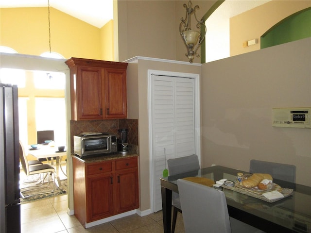 kitchen with high vaulted ceiling, light tile patterned floors, stainless steel fridge, pendant lighting, and decorative backsplash