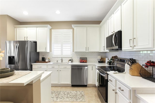 kitchen with appliances with stainless steel finishes, sink, backsplash, light tile patterned flooring, and white cabinetry