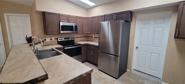 kitchen with dark brown cabinetry, sink, light tile patterned floors, and appliances with stainless steel finishes