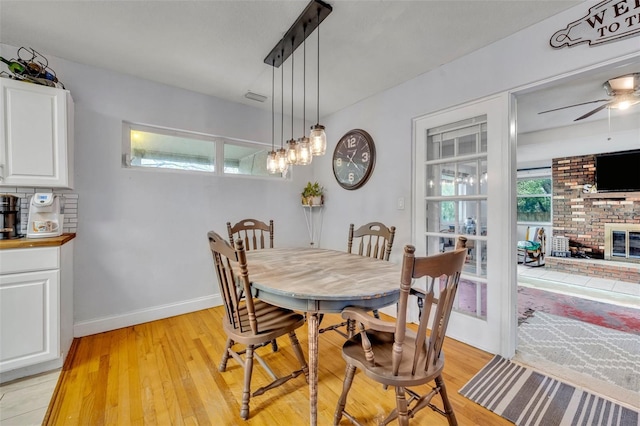 dining room with a brick fireplace, ceiling fan, and light hardwood / wood-style flooring