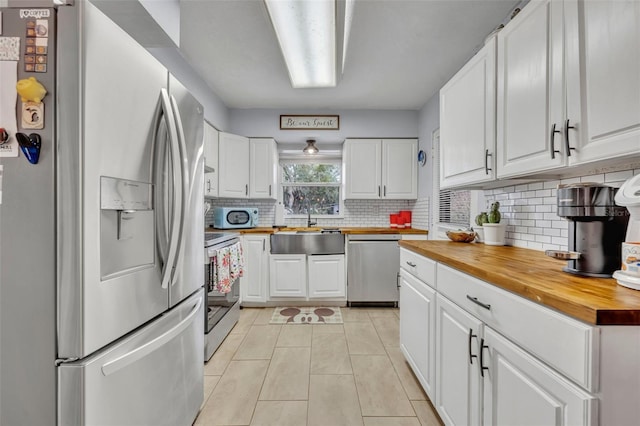 kitchen featuring sink, butcher block countertops, light tile patterned floors, stainless steel appliances, and white cabinets