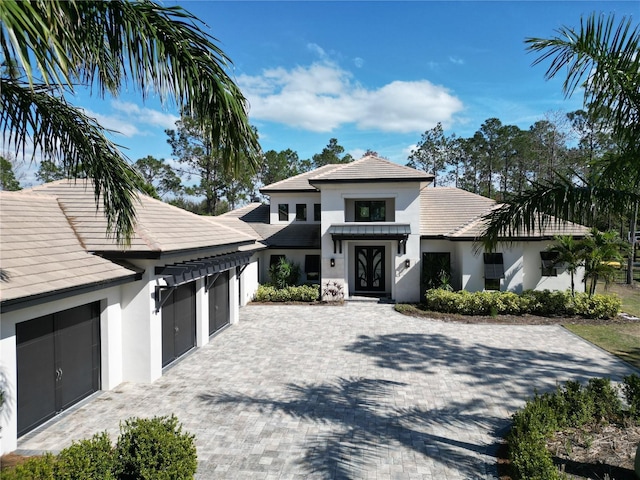 view of front of house featuring decorative driveway, an attached garage, a tile roof, and stucco siding