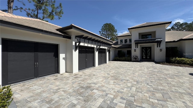 exterior space featuring decorative driveway, a tile roof, an attached garage, and stucco siding