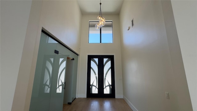 foyer entrance with baseboards, wood finished floors, a high ceiling, french doors, and a notable chandelier