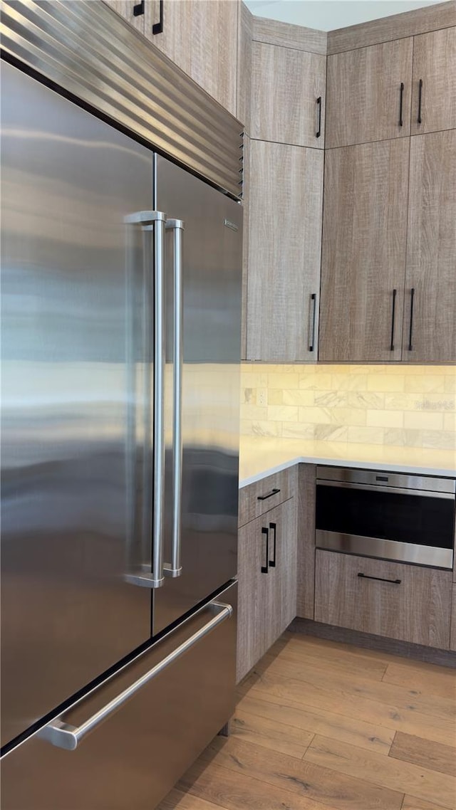 kitchen with light wood-type flooring, modern cabinets, stainless steel built in refrigerator, and backsplash