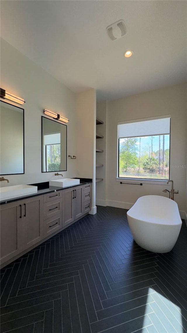 bathroom with a freestanding bath, double vanity, a sink, and baseboards