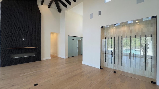 empty room with an accent wall, visible vents, wood finished floors, and beamed ceiling