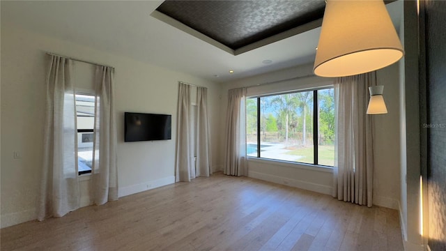 unfurnished living room featuring a raised ceiling, light wood-style flooring, and baseboards