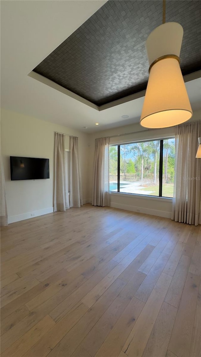 unfurnished living room with a tray ceiling, baseboards, and hardwood / wood-style flooring