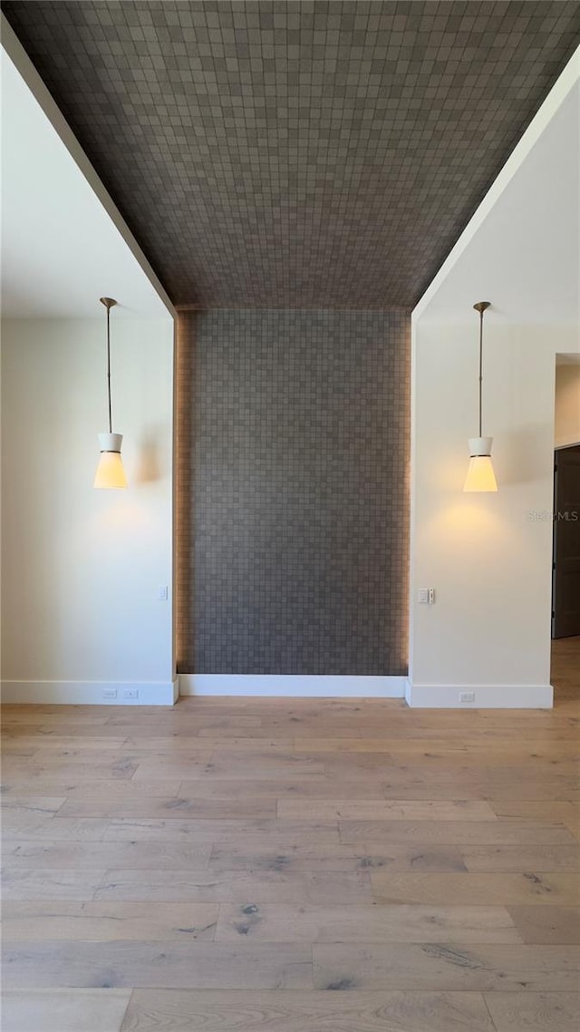 empty room with an accent wall, light wood-type flooring, and baseboards