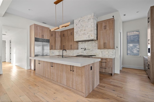 kitchen featuring stainless steel appliances, light countertops, decorative backsplash, light wood finished floors, and a center island with sink