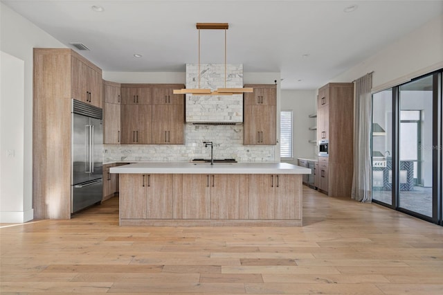 kitchen featuring built in refrigerator, a sink, light countertops, light wood-type flooring, and decorative backsplash