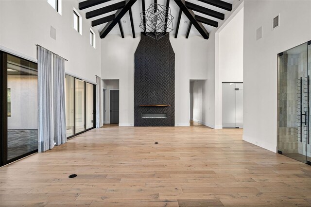 unfurnished living room featuring visible vents, wood finished floors, a high ceiling, a chandelier, and beam ceiling