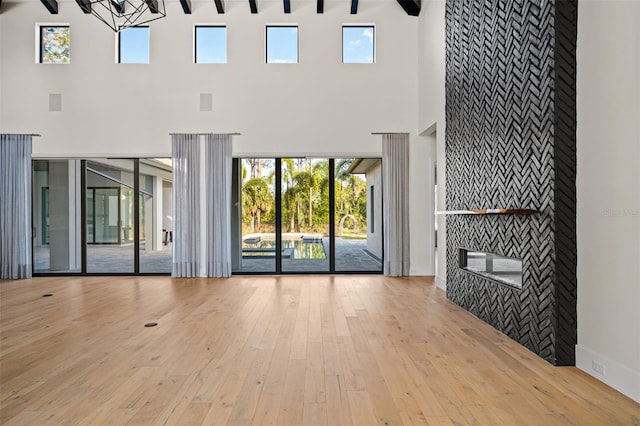 unfurnished living room with wood-type flooring, a high ceiling, beamed ceiling, and a multi sided fireplace