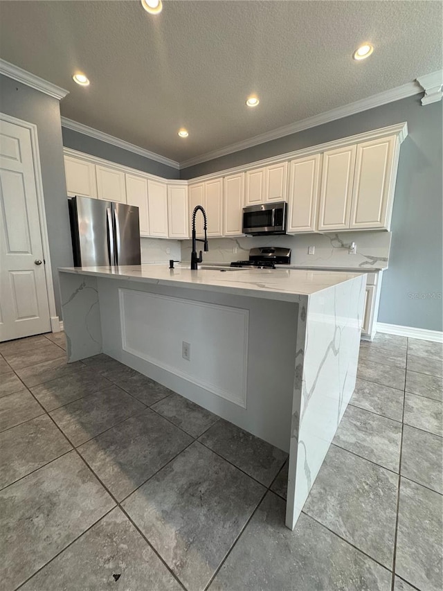 kitchen featuring ornamental molding, an island with sink, white cabinets, and appliances with stainless steel finishes