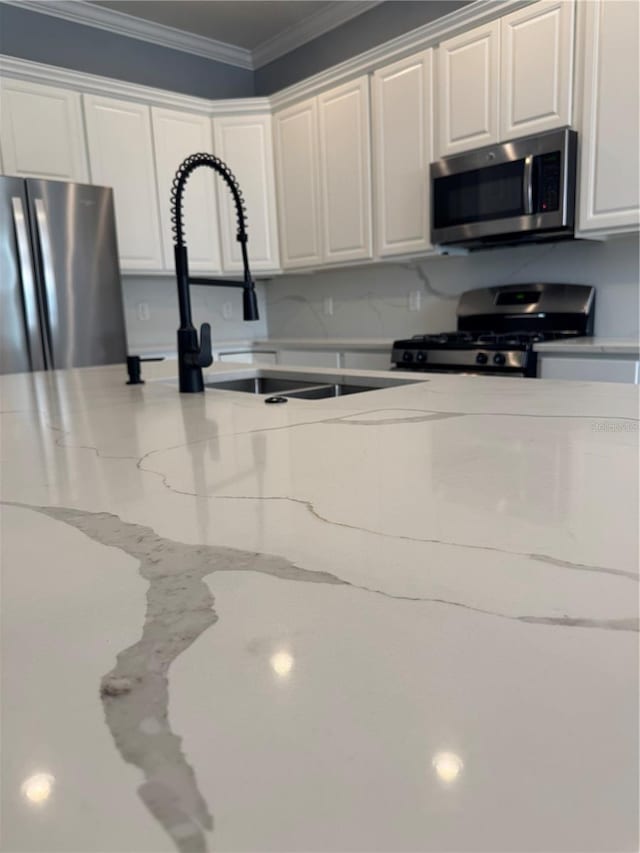 kitchen featuring sink, white cabinetry, light stone counters, ornamental molding, and appliances with stainless steel finishes