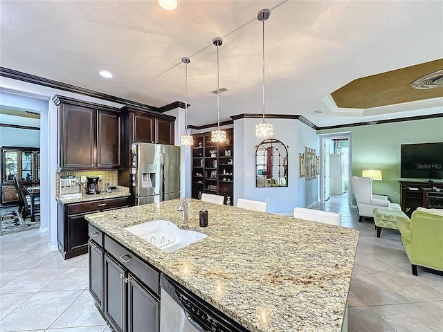 kitchen featuring sink, hanging light fixtures, an island with sink, stainless steel appliances, and light stone countertops