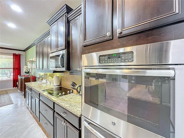 kitchen with light stone counters, light tile patterned floors, ornamental molding, appliances with stainless steel finishes, and decorative backsplash