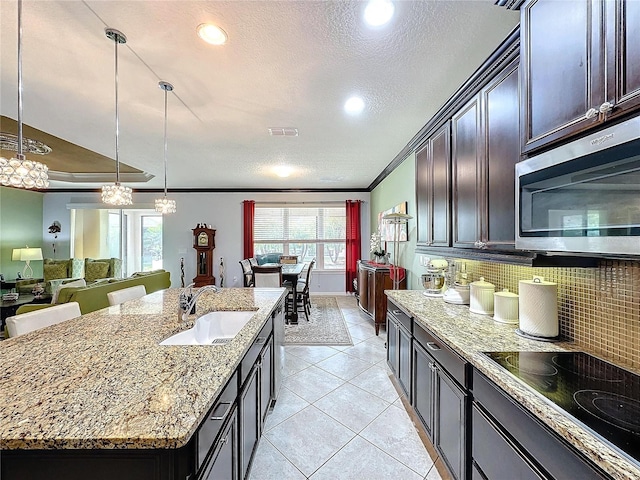 kitchen featuring sink, decorative backsplash, ornamental molding, a center island with sink, and black electric cooktop