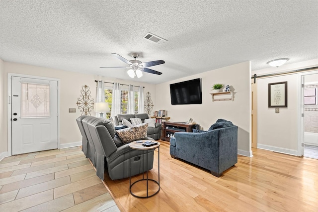 living room with a textured ceiling, light hardwood / wood-style floors, a barn door, and ceiling fan