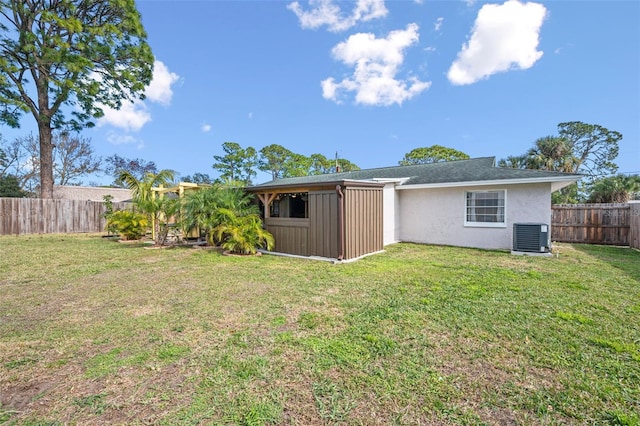 rear view of house with central AC unit and a lawn