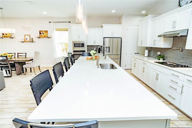 kitchen with decorative light fixtures, an island with sink, white cabinetry, sink, and stainless steel appliances