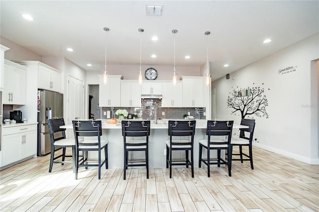 kitchen with an island with sink, white cabinets, and decorative light fixtures