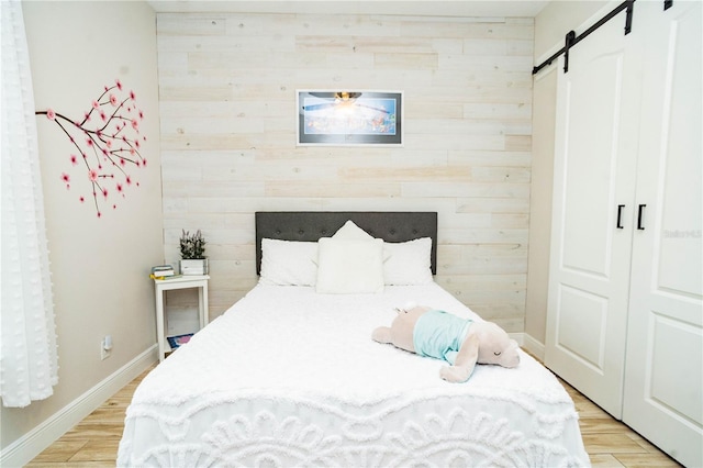 bedroom featuring wood walls, a barn door, and light wood-type flooring