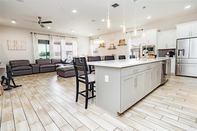 kitchen with appliances with stainless steel finishes, an island with sink, hanging light fixtures, and white cabinets