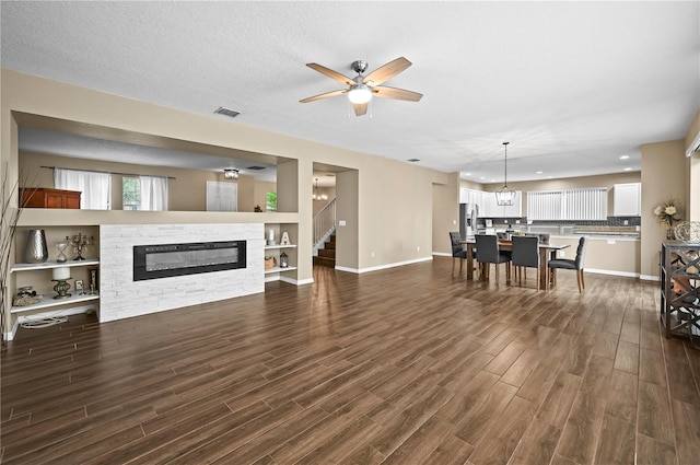 living room with dark wood-type flooring, ceiling fan, a fireplace, and a textured ceiling