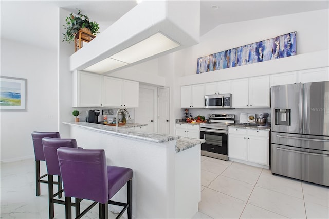 kitchen featuring light stone counters, appliances with stainless steel finishes, a kitchen breakfast bar, kitchen peninsula, and white cabinets