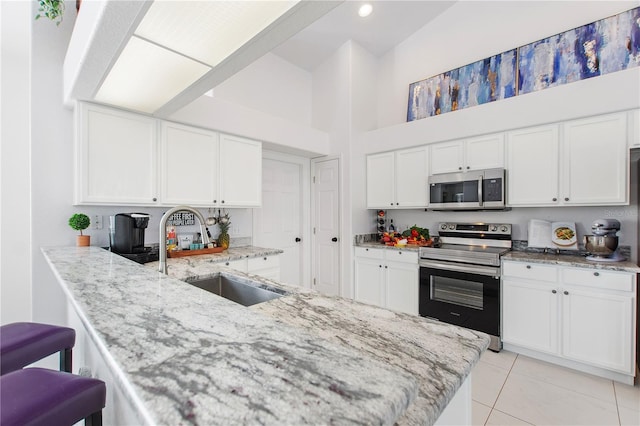 kitchen featuring sink, stainless steel appliances, light stone counters, white cabinets, and kitchen peninsula