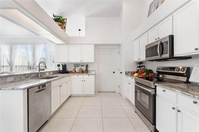 kitchen with sink, light stone counters, light tile patterned floors, appliances with stainless steel finishes, and white cabinets