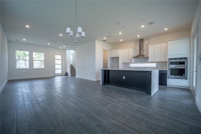 kitchen with stainless steel double oven, light countertops, white cabinetry, wall chimney range hood, and tasteful backsplash