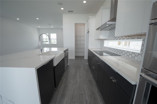 kitchen with wall chimney range hood, decorative backsplash, wood finished floors, black electric cooktop, and dark cabinets